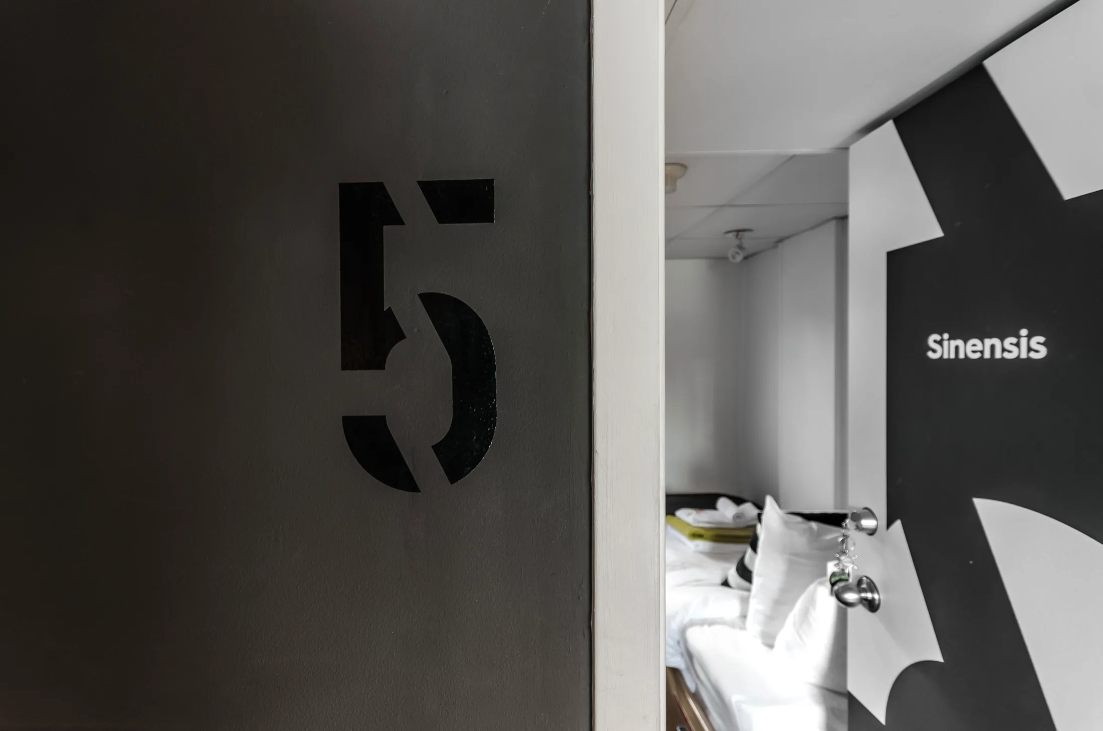 A cabin door numbered 5 in stencilled black, open onto a made-up berth, with the species name Sinensis set in white across the water-lily silhouette on the wall beyond.