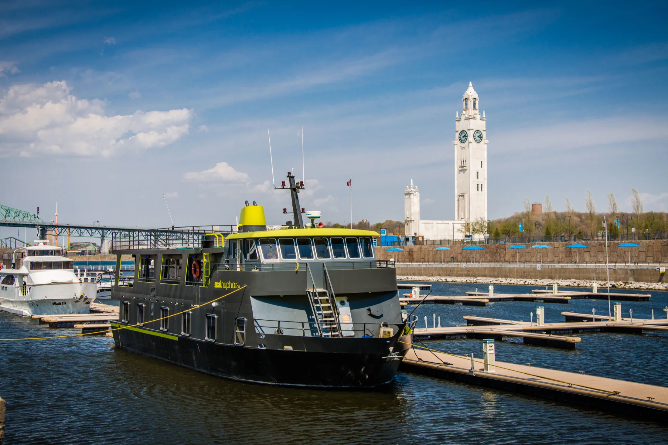 The Skal Nuphar moored in the Old Port of Montreal, its black hull and yellow-green trim set against the white Clock Tower and a row of empty docks.